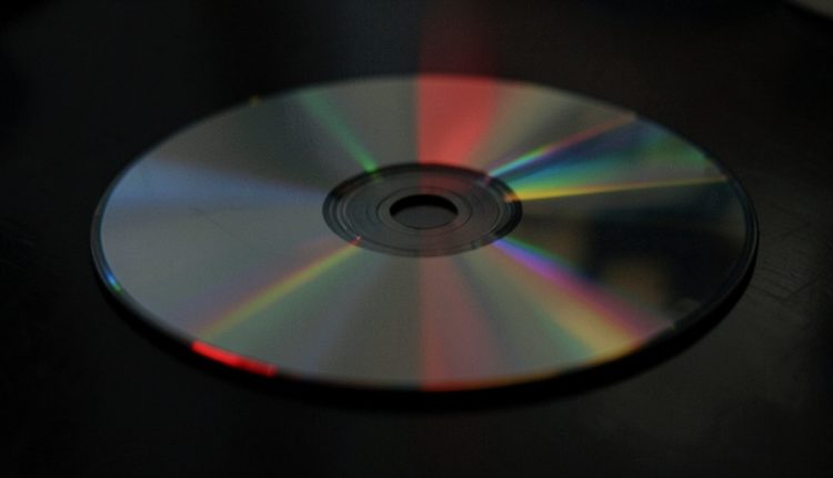 A compact disc on a dark surface scattering rainbow light across its underside with a faint red glow