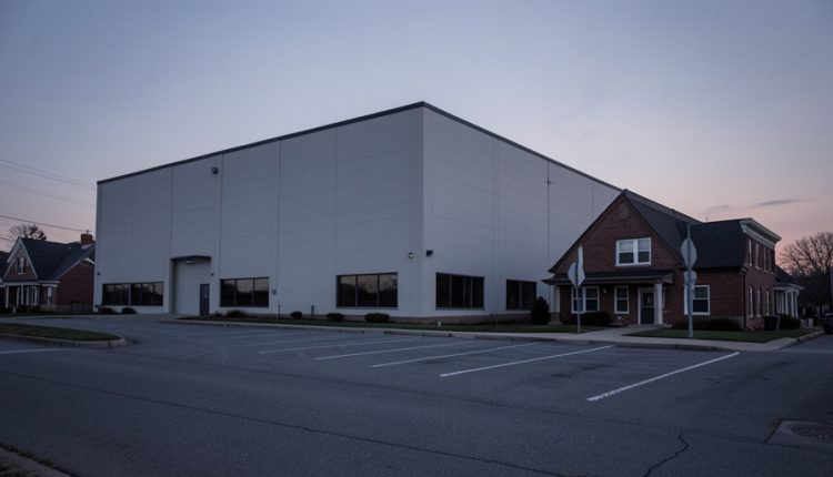 Large windowless data center building beside a small town street with an empty parking lot at dusk
