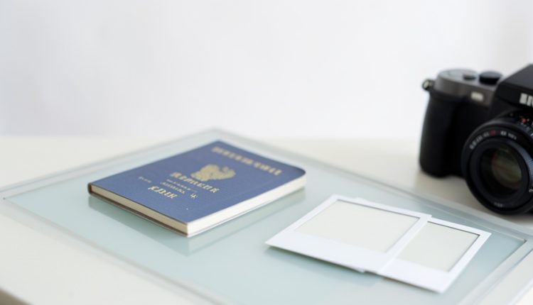 A passport book beside blank square photo prints and a camera on a light table